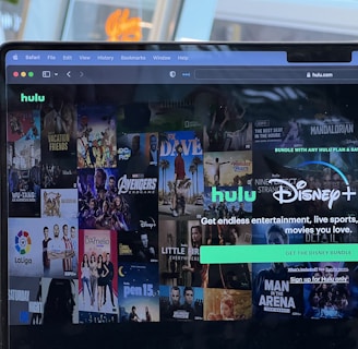 A laptop screen displays a web page featuring a mix of movie and TV show covers, highlighting popular titles and a Hulu and Disney+ bundle promotion. There are visible icons and images of films and shows alongside promotional text offering entertainment and live sports.