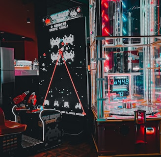 An arcade setting featuring a classic Space Invaders game setup and a modern gaming machine with seats. Bright neon lights illuminate the area, with scores displayed on digital screens. A bright and visually engaging environment full of electronic components.